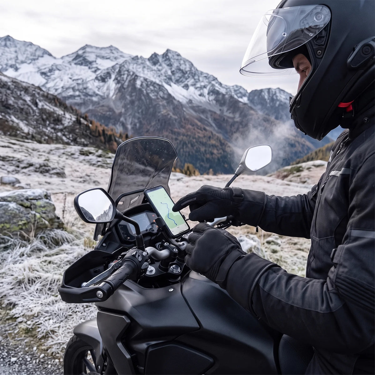 Rider tapping the GPS on the handlebar with a gloved finger at an alpine pass in fall